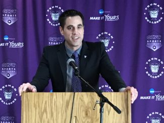Jeff Horner behind a podium with a purple curtain behind him, for a press conference